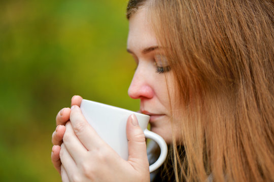 Close Up. Girl With A Red Nose Drinking Hot Tea From A White Mug. Cold Girl. The Girl Is Sick With A Runny Nose Drinking Cure. Redheaded Woman. Horizontal Photography