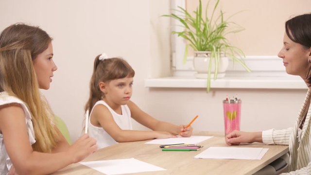 Child psychologist working with two little girls, children draw with colored pencils. Cheerful young therapist using picture interpretation technique