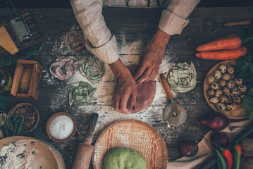 Making homemade pasta linguine on rustic kitchen table with flour, rolling pin and vegetables. Rustic style, toned image.
