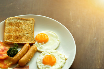 Top view of American breakfast on dark brown wooden table with sun flare background.