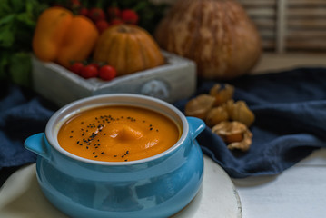 Homemade autumn butternut squash soup with bread. Roasted pumpkin and carrot soup with cream and pumpkin seeds on white wooden background. Concept of healthy eating food. Copy space. Toned image.