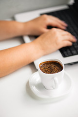 Cup of coffee at coffee shop table and and woman working on laptop. Typing female hands on keyboard. Morning routine at workplace