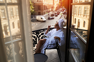 Beautiful blonde in a white coat enjoying a glass of white wine sitting on a hotel terrace against