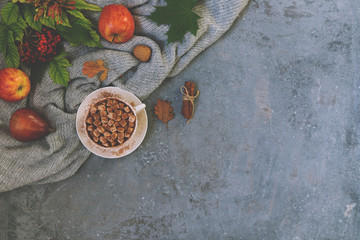 Autumn background. A mug of coffee on the dark background with yellow falling leaves, red berries and cones. Hello autumn. Instagram fashion drink composition. Toned image. Top view, copy space.