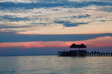 silhouettes of wooden pier and people at tropical sunset