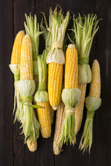 A pile of ripe ears of corn for grilling on a wooden background. Top view. BBQ Independence Day, BBQ Thanksgiving.