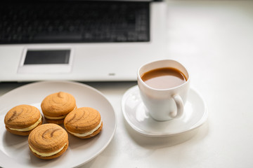 Business coffee break, sweet treats, morning at office workplace. Cup of coffee and cookies and laptop on table