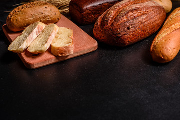 Fresh fragrant bread with grains and cones of wheat against a dark background. Assortment of baked bread on wooden table background. Fresh fragrant bread on the table. Food concept. 