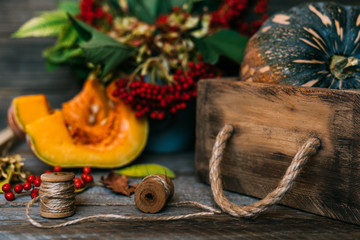 Autumn background with red berries with green leaves, pumpkins in the vintage wooden box. Fall harvest on aged wood with copy space. Mockup for seasonal offers and holiday post card. Toned image.