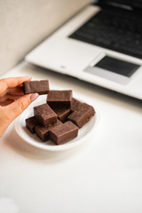 Unhealthy eating habits, snacking and deadline. Young stressed woman eating sweets at office workplace. Girl taking chocolate candy from plate on a desktop. Stress and junk food concept