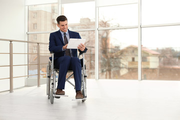 Fototapeta na wymiar Young businessman in wheelchair using tablet near window indoors