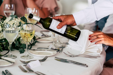 Unrecognizable people at. work in restaurant or event celebration catering - hand of a waiter serving. whit wine to a lady at the table - luxury and work job concept