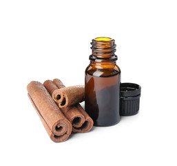 Bottle of essential oil and cinnamon sticks on white background