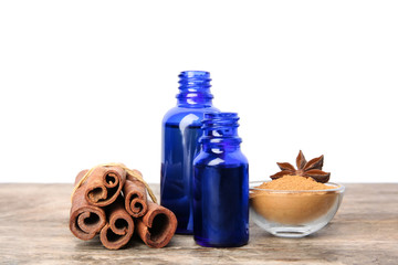 Bottles of essential oils, cinnamon sticks and powder on wooden table against white background