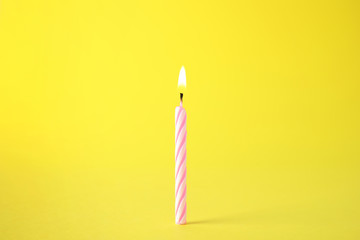 Burning pink striped birthday candle on yellow background