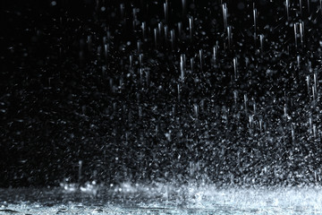 Fototapeta na wymiar Heavy rain falling down on ground against dark background