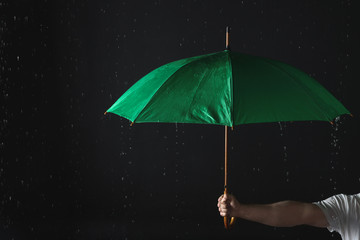 Man holding green umbrella under rain against black background, closeup