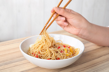 Woman eating cooked Asian noodles with chopsticks at table, closeup