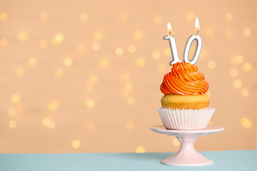Birthday cupcake with number ten candle on stand against festive lights, space for text