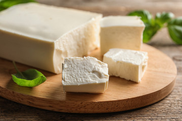 Board with feta cheese and basil on wooden table, closeup