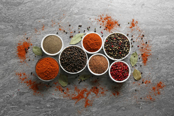 Different ground pepper and corns on grey table, flat lay