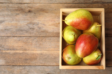 Fototapeta na wymiar Crate with ripe juicy pears on brown wooden table, flat lay. Space for text