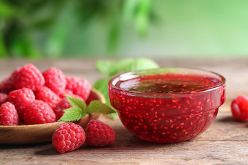 Bowl of sweet jam with ripe raspberries on wooden table, closeup