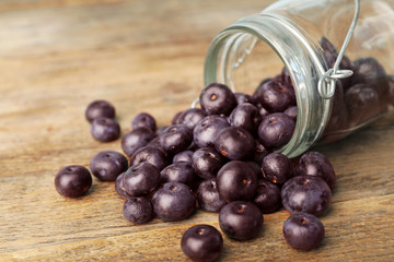 Fresh acai berries scattered from jar on wooden table, closeup view. Space for text