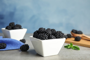 Fototapeta na wymiar Bowls of tasty blackberries on grey table against blue background