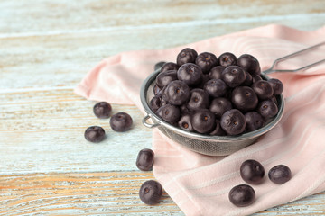 Metal sieve of fresh acai berries on light wooden table, closeup. Space for text