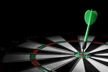 Green arrow hitting target on dart board against black background. Space for text