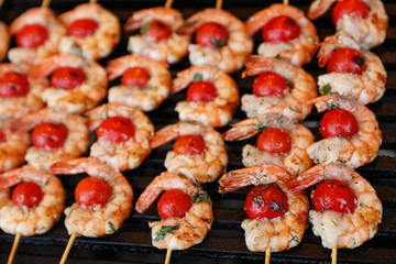Delicious fresh shrimp skewers with cherry tomatoes on grill, closeup