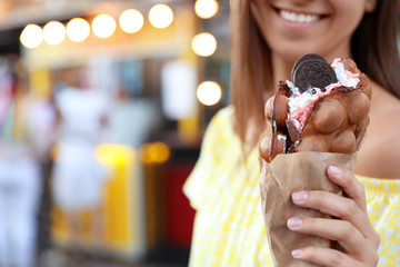 Young woman holding delicious sweet bubble waffle with ice cream outdoors, closeup