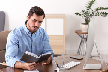 Handsome young man working with notebook and computer at table in office