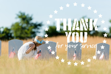 cute kid sitting near headstone with american flag in graveyard with thank you for your service...