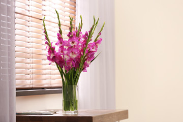 Vase with beautiful pink gladiolus flowers on wooden table in room, space for text
