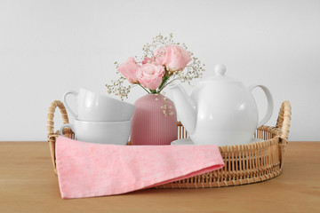 Tray with ceramic tea set and beautiful bouquet on wooden table