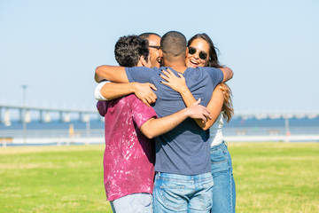 Happy smiling friends hugging in circle. Group of cheerful people laughing while standing close to each other in park. Union concept
