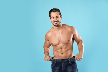 Young man with slim body in old big size jeans on light blue background. Space for text