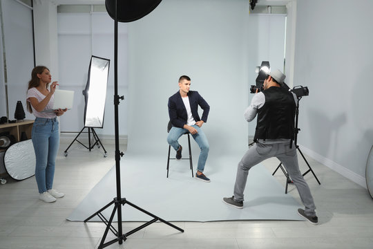 Professional photographer with assistant taking picture of young man in modern studio