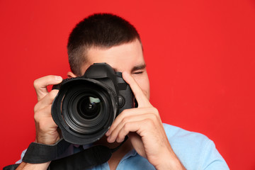 Fototapeta premium Young professional photographer taking picture on red background