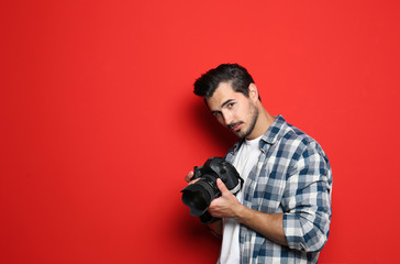 Young photographer with professional camera on red background. Space for text