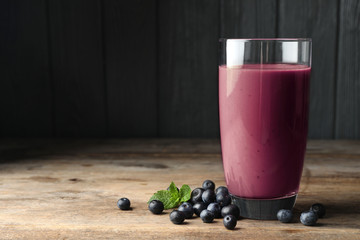 Tasty acai drink in glass and berries on wooden table. Space for text