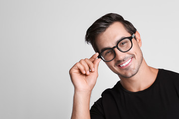 Portrait of handsome young man in black t-shirt with glasses on grey background. Space for text