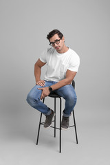 Handsome young man sitting on stool against grey background