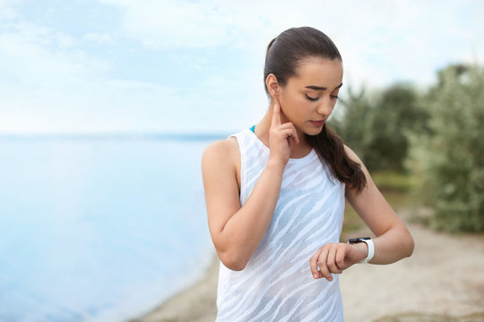 Young woman checking pulse after training on beach. Space for text