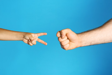 Little child and his father playing rock, paper and scissors on blue background, closeup