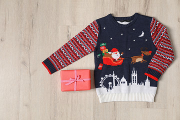 Warm Christmas sweater and gift box on light wooden table, flat lay
