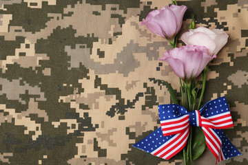 Top view of flowers and ribbon bow with American flag pattern on camouflage background, space for...