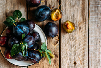 Fresh pile of plums in a old bowl on rustic table with green leaf. Toned image. Soft focus. Copy space.